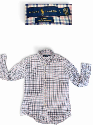 Rutig skjorta från Ralph Lauren - Klassisk långärmad skjorta från Ralph Lauren i slim fit-modell. Skjortan har ett rutigt mönster i blått, rött och vitt samt button-down krage. Tillverkad i stretch oxford-tyg för extra komfort. Ikoniska loggan broderad på bröstet.