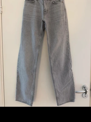 Ljusgrå raka jeans - Säljer ett par ljusgrå jeans med rak passform och medelhög midja. Jeansen har klassisk femficksdesign och är tillverkade i denim. Perfekta för en avslappnad och trendig look.