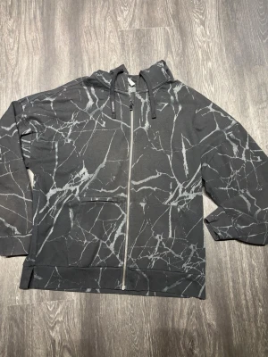 Gymshark Power Zip Hoodie Black Print SS22  - Gymshark Power Zip Hoodie – Black Print, SS22 (2022). Unik svart/grå all-over jacquard-design med broderad Gymshark-logga på bröstet, full dragkedja och justerbar huva med Gymshark-detaljer. Kraftigt premiumtyg med atletisk passform och exklusiv känsla. En äldre Gymshark-modell som inte längre säljs. Skicket är som nytt – extremt välbevarad.