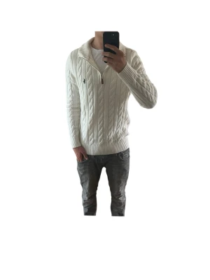 Vit kabelstickad tröja Polo Ralph Lauren - Vit kabelstickad tröja från Polo Ralph Lauren i Storlek Mmed halv dragkedja och hög krage. Tröjan har ribbade muddar och nederkant samt den klassiska broderade loggan på bröstet. Perfekt för lager på lager och riktigt snygg till jeans. Modellen på bilden är 180cm och väger 69kg, och bär vanligtvis storlek M. Skriv vid minsta fundering. Fraktas snabbt📦