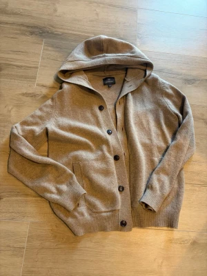 Beige stickad hoodie med knappar - Mysig beige stickad kofta med huva och knäppning framtill. Extremt bekväm hoodie men som tyvärr inte kommit till användning väldigt bra skick!!