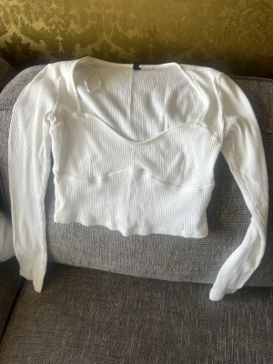 Vit ribbad långärmad crop top - Säljer en vit ribbad crop top med långa ärmar och rundad urringning. Toppen har en figurnära passform och är tillverkad i ett stretchigt material som ger en snygg siluett. Perfekt att matcha med höga jeans eller kjol.
