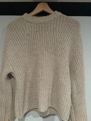 Beige chunky stickad tröja - Säljer en beige chunky stickad tröja med grov struktur och avslappnad passform. Tröjan har rund halsringning och långa ärmar. Perfekt för lager på lager och riktigt mysig till hösten. Garnet har små detaljer av färg i sig men övrigt beige.