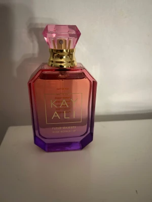Kayali Fleur Majesty parfym - Kayali Fleur Majesty Rose Royale 31 är en parfym i en lyxig glasflaska med rosa till lila färgskiftning och gulddetaljer. Flaskan har en elegant, multifasetterad kork i rosa plast och en fyrkantig form med guldtext på framsidan.