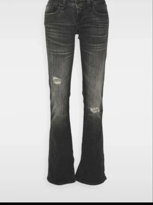 Grå bootcut jeans med slitningar - Snygga grå bootcut jeans med slitna detaljer på låren och knäna. Jeansen har en klassisk femficksmodell och lätt tvättad look som ger en cool vintagekänsla. Perfekta för dig som gillar en avslappnad och trendig stil. Jeansen är i storlek w26 l32. De är i mycket bra skick. Jeansen är väldigt populära och även slutsålda.
