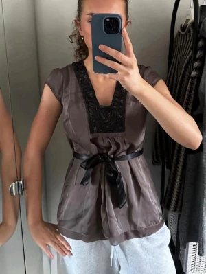 Brun topp med spetsdetaljer - Snygg brun tunika med korta ärmar och djup v-ringning dekorerad med svart spets. 