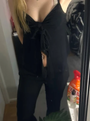 Svart omlottopp med knyt - Snygg svart omlottopp med knyt framtill och djup v-ringning. Toppen är ärmlös och har en croppad passform som visar lite mage. Perfekt för dig som vill ha en trendig och enkel topp till din outfit.