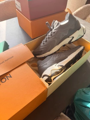 Grå Louis Vuitton sneakers - Snygga grå sneakers från Louis Vuitton med chunky vit och svart sula. Skorna har LV-detaljer på sidan, meshpaneler och coola former i designen. Perfekta för dig som vill ha en exklusiv och trendig look.