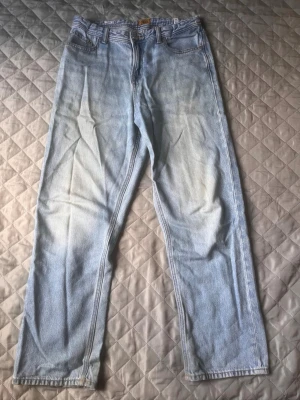 Ljusblå raka jeans i denim - Säljer ett par ljusblå jeans med rak passform och klassisk femficksdesign. Jeansen har hög midja och är tillverkade i ett slitstarkt denimtyg. Perfekta  för en avslappnad och trendig look.