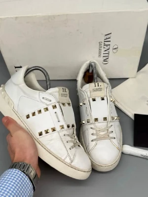 Valentino vita sneakers med nitar - Säljer ett par vita sneakers från Valentino Garavani med ikoniska guldfärgade nitar runt hela skon. Skorna är låga och har en chunky sula samt detaljer i vitt läder. Klassisk snörning framtill och cool design som sticker ut.Säljer mina valentinos, dom har handtvättats så det är betydligt renare nu. Originalbox, dustbag, och ett par extra snören kommer med 🥰 Nypris ca 8000kr Den har gått igenom verifieringstjänst. Skriv för frågor 🦄🦄