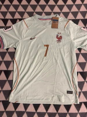 Ljusblå Frankrike fotbollströja Nike - Säljer en ljusblå officiell Frankrike fotbollströja från Nike med nummer 7 på bröstet. Tröjan har broderad tupp-logga, två stjärnor ovanför, och tunna orange detaljer längs sidorna. Korta ärmar och rund hals med trikolor-detalj på insidan.
