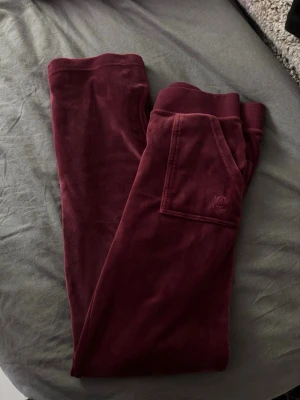 Juicy Couture vinröda velourbyxor Y2K – XS - Vinröda Juicy Couture velourbyxor i mjuk sammet ❤️ Raka ben, snörning i midjan och snygga fickdetaljer baktill. Väldigt fin mörk vinröd färg och perfekt Y2K/vintage vibe. Storlek XS. Fint skick.