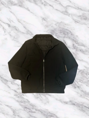 Cadigan från Zara - Stilren svart cardigan från Zara med hel dragkedja framtill och hög krage. Jackan har lång ärm och enkel design som passar till många olika outfits. Perfekt för kyligare dagar och ger en clean look.