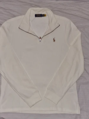 Ralph Lauren  Vit halvzip tröja - Klassisk vit långärmad  med halv dragkedja och broderad logga på bröstet. Tröjan har hög krage och ribbade muddar vid ärmslut och nederkant. Perfekt för en clean och stilren look. Sitter som M