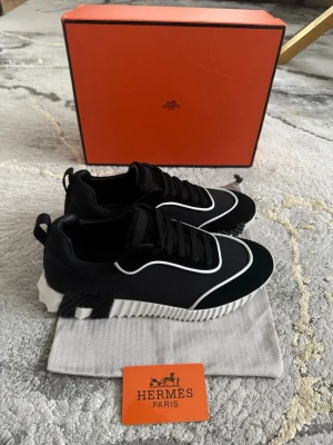 Svarta H sneakers med vit sula - Snygga svarta H  sneakers med vita detaljer och en chunky, räfflad vit sula. Skorna har svarta skosnören och en modern design med kontrasterande vita linjer längs ovandelen. Perfekta för dig som vill ha en exklusiv och trendig look.
