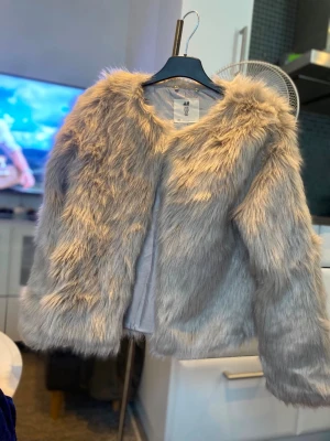 Ljusgrå fluffig pälsjacka H&M - Säljer en supermjuk och fluffig ljusgrå pälsjacka från H&M. Jackan har rund halsringning, långa ärmar och är helfodrad. Perfekt för dig som vill ha en trendig och varm look under vintern. Stängs framtill utan synliga knappar eller dragkedja.