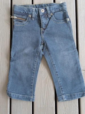 Blå raka jeans med dragkedjedetalj barn stl 80 - Snygga blå jeans i rak modell med klassiska fem fickor och en cool dragkedjedetalj vid ena fickan. Jeansen har normal midja, bälteshällor och är gjorda i mjukt denimtyg. Perfekta för en avslappnad och trendig look.