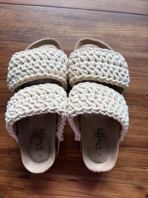 Beige flätade sandaler från Duffy - Snygga sandaler från Duffy i beige med två breda, flätade band i textil. Mjuk innersula och öppen tå ger en avslappnad och trendig look. Perfekta för varma dagar och passar till många olika outfits.