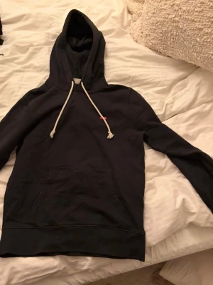 Svart hoodie från Levi's med snörning - Säljer en svart hoodie från Levi's i standard fit. Hoodien har vit snörning i huvan, känguruficka framtill och en liten röd Levi's-tag på bröstet. Perfekt för dig som gillar enkel och stilren streetwear.
