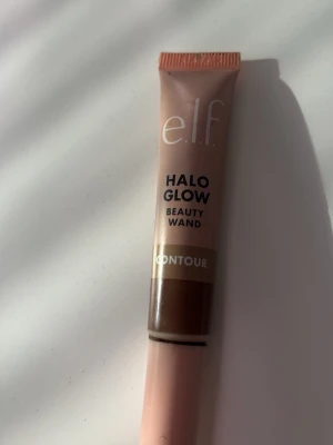 e.l.f. Halo Glow Beauty Wand Contour - Flytande bronzer från e.l.f. i färgen Medium/Tan. Kommer i en smidig tub med applikator och ger en naturlig glow och kontur till ansiktet. Perfekt för att skapa definierade drag och en solkysst look.