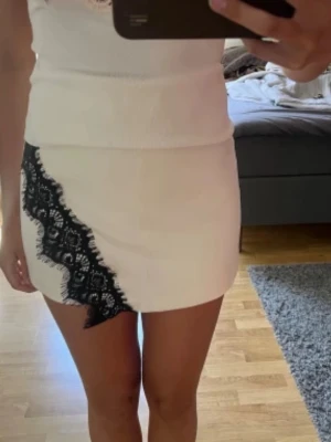Vit minikjol med svart spetsdetalj - Säljer en vit kortkjol med svarta spetsdetaljer, det är kjol vid framsidan och shorts på baksidan. Väldigt bekvämt perfekt inför hösten med en stickad tröja. Den är helt ny med prislappen kvar, den är helt oanvänd. Skriv mig frågor 