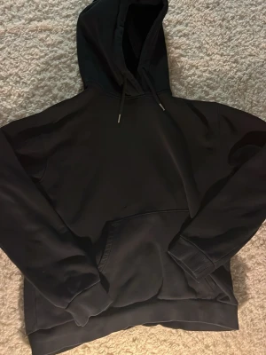 Svart hoodie från RYVL - En stilren svart hoodie från RYVL med huva och dragsnören. Klassisk känguruficka framtill och ribbade muddar vid ärmar och nederkant. Perfekt för en avslappnad look och enkel att matcha med det mesta passar folk som e 170 plus .
