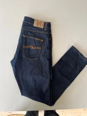 Mörkblå dry denim jeans från Nudie - Säljer ett par nästan helt nya dry denim jeans från nudie. Inga hål eller andra defekter. Med mycket användning kommer dem att få många fina fades. Storlek 32W 32L men sitter mer som en 30W. Om du har frågor om till exempel storlek eller annat är det bara att säga till Mvh Olof!