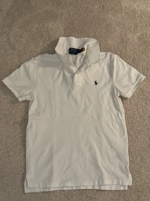 Vit kortärmad skjorta Polo Ralph Lauren - Vit kortärmad skjorta från Polo Ralph Lauren med klassisk krage, knappar vid halsen och broderad mörkblå logga på bröstet. Tillverkad i mjuk bomull för en clean och tidlös stil.