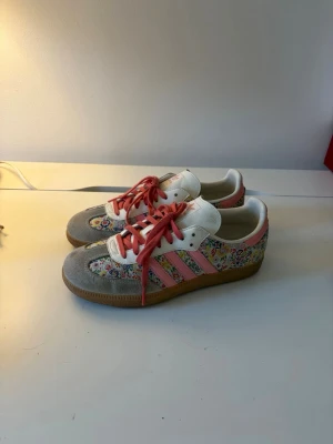 Blommiga Adidas sneakers med rosa detaljer - Unika Adidas sneakers med blommigt tyg, rosa ränder och snören samt beige och grå mockadetaljer. Säljer ur garderoben så först till kvarn! De är i storlek 38,5 men saknar innersulorna. Skriv vid funderingar!👍
