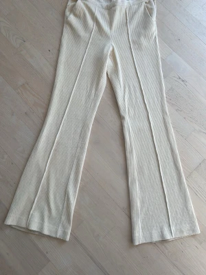 Ribbade beige leggings med utsvängda ben - Säljer ett par ribbade leggings i ljusbeige färg med utsvängda ben och hög midja. Materialet är stretchigt och mjukt, perfekt för en chill och trendig look. Snygga sömdetaljer framtill ger extra stilpoäng.