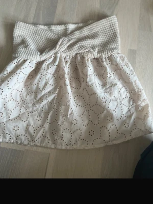 Beige topp med broderade blommor - Söt beige topp med bred, ribbad midja och broderade blommor i tyget. Toppen har en luftig och lätt känsla, perfekt för varmare dagar.