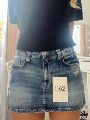 Blå jeanskjol med slitningar - Säljer en supersnygg blå jeanskjol från Stradivarius i kort modell med trendiga slitna detaljer. Kjolen har inbyggda shorts, vilket gör den både bekväm och praktisk. Jag är 165cm lång och brukar oftast ha storlek 36 så du får en lite uppfattning om hur den sitter på mig. 