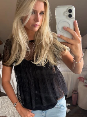 Svart prickig blus - Säljer en svart transparent blus med prickigt mönster och volangdetaljer. Blusen har korta ärmar och rund halsringning. Perfekt att styla med ett linne under för en trendig look. Blusen väldigt genomskinlig men jag brukar använda den med ett linne under (se bild 1&2) så tycker jag den blir jättefin