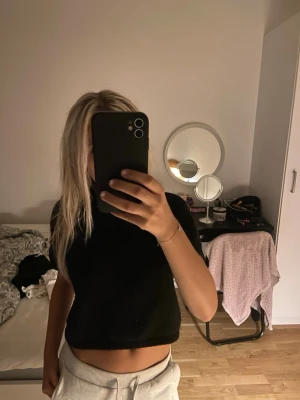 Svart croppad stickad topp - Säljer en svart croppad stickad topp med korta ärmar och rund hals. Perfekt till höga byxor eller kjol för en chill och snygg look. Enkel och stilren design som passar till mycket.