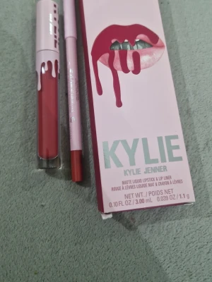 Kylie Jenner matt läppstift & lip liner - Säljer ett set med matt flytande läppstift och matchande lip liner från Kylie Jenner. Färgen är en varm, rosabrun nyans. Läppstiftet kommer i en genomskinlig tub med rosa lock och vit text, medan pennan är ljusrosa med färgad spets. Perfekt för en snygg och definierad look.