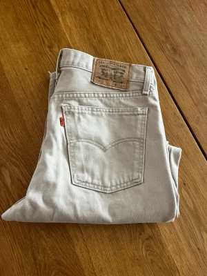 Beiga raka jeans från Levi's - Snygga ljusbeiga jeans från Levi's med klassisk rak passform. Jeansen har den ikoniska läderlappen bak i midjan och orange Levi's-tagg på bakfickan. 