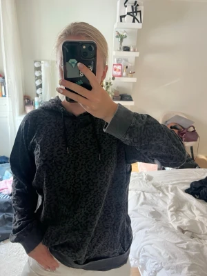 Grå leopardmönstrad hoodie från Zizzi - Säljer en grå hoodie från Zizzi med snyggt leopardmönster. Hoodien har huva med dragsko och ribbade muddar vid ärmslut och nederkant. Perfekt för dig som gillar djurmönstrat och vill ha en chill och trendig stil.