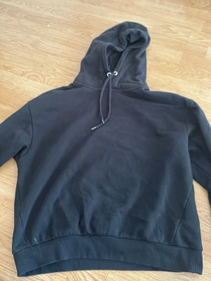 Svart hoodie med dragsko - En enkel svart hoodie med huva och dragsko. Hoodien har ribbade muddar vid ärmslut och nederkant samt en klassisk passform. Perfekt för en avslappnad och stilren look.