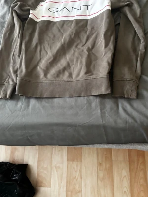 Beige sweatshirt från GANT - Snygg beige sweatshirt från GANT med vit panel och logga framtill. Tröjan har ribbade muddar vid ärmslut och nederkant samt en avslappnad passform. Perfekt för en casual och stilren look.