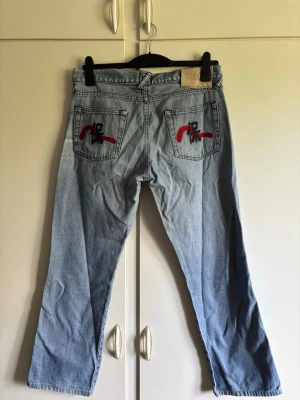 Unika Evisu Ljusblå Jeans - Tja, säljer nu mina unika Vintage Evisu jeans billigt! De har riktigt coolt mönster på bakfickorna och snygga slitningar. Dom är i storlek 32 med en blandning på typ straight/Loose/bootcut passform. Hör av er vid frågor eller funderingar!😄p.s. ser ganska skrynkliga ut på bilderna men det är dels jag som suger på att ta bild och det syns inte när jeansen sitter på benen👍🏻