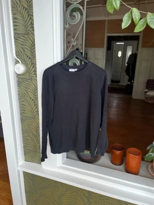 Svart långärmad tröja - En enkel och stilren svart långärmad tröja med rund hals. Tröjan har en rak passform och är perfekt för dig som gillar minimalistisk stil. Passar till det mesta och är lätt att matcha med andra plagg.