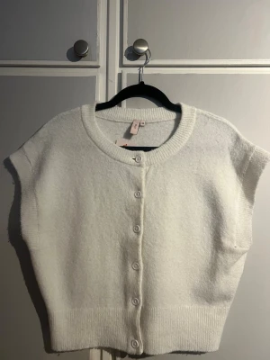 Vit stickad kortärmad tröja - Säljer en vit stickad tröja med korta ärmar och rund hals. Tröjan har knappar framtill och bred ribbad kant nedtill samt vid halsen. Den har även lite vidare öppning vid armarna (se bild 4)Materialet ser mjukt och fluffigt ut, perfekt inför hösten. Prislappen kvar, aldirg använd!Skriv vid frågor eller funderingar