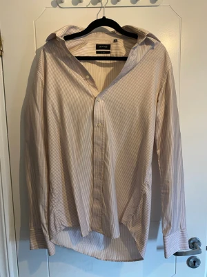 Randig skjorta från Sand - Säljer en klassisk långärmad skjorta från Sand med tunna ränder i ljusa toner. Skjortan har knappar framtill och en tidlös krage. Perfekt för en stilren look och tillverkad i ett mjukt material.