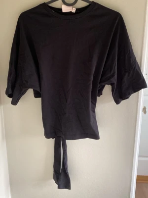 Svart croppad topp med knyt - Säljer en svart croppad topp med vida ärmar och knytband i midjan. Toppen har en enkel och stilren design, perfekt för att matcha med höga jeans eller kjol. Tillverkad i mjuk bomull för en bekväm känsla.