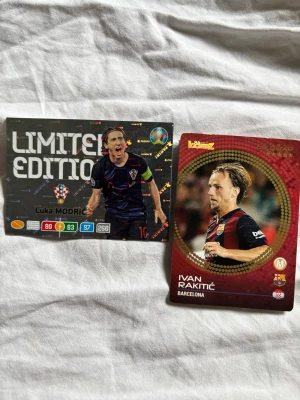 Fotbollssamlarbilder Modric & Rakitic - Två samlarkort med fotbollsspelarna Luka Modric och Ivan Rakitic. Ena kortet är en Limited Edition med holografiska detaljer och statistik, det andra är ett klassiskt kort med röd och svart design. Perfekt för dig som gillar att samla fotbollskort.