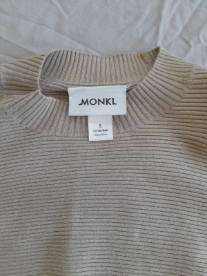 Beige ribbad stickad tröja Monki - Säljer en beige ribbad stickad tröja från Monki i storlek S. Tröjan har en croppad passform, långa ärmar och rund halsringning. Perfekt för dig som gillar en enkel men trendig look. Materialet är mjukt och stretchigt för extra komfort.
