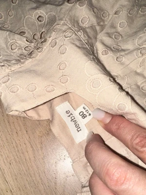Beige broderad klänning från Newbie - Söt beige klänning från Newbie med broderade blommor och kort ärm. Klänningen har volang nertill och en luftig passform, perfekt för varmare dagar. Tillverkad i mjuk bomull med fina detaljer och rund halsringning.Beige broderad klänning från Newbie