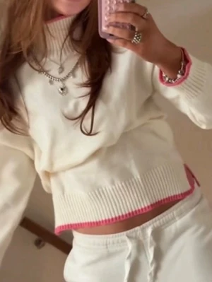 Vit stickad tröja Filippa montankollektion - Säljer en krämvit stickad tröja med ribbade muddar och rosa detaljer vid ärmslut och nederkant. Tröjan har en hög hals och avslappnad passform, perfekt för en chill och trendig look. Materialet ser mjukt och bekvämt ut.