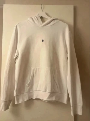 Vit Ralph Lauren hoodie - Säljer en stilren vit hoodie från Polo Ralph Lauren med den klassiska broderade loggan på bröstet. Den är i toppen skick förutom den pyttelilla defekten ni kan se på sista bilden som knappt märks. Storlek 18/20 barnstorlek vilket motsvarar en S eller eventuellt en mindre M. Vid några frågor eller funderingar är det bara att höra av sig.