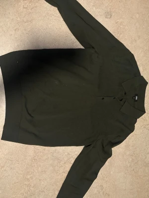 Mörkgrön stickad pikétröja Uniqlo - Snygg mörkgrön stickad pikétröja från Uniqlo med krage och knäppning framtill. Tröjan har långa ärmar och ribbade muddar vid ärmslut och nederkant. Perfekt för dig som gillar stilrena och enkla plagg.